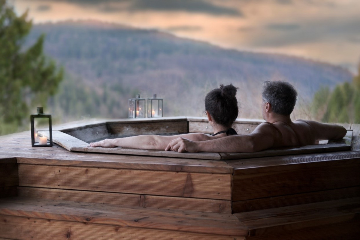Man and woman sitting in an outdoor hot tub facing sunset and mountains