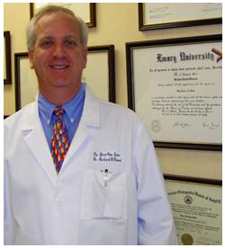 Dr. Kimmel standing by certificates on wall Logo