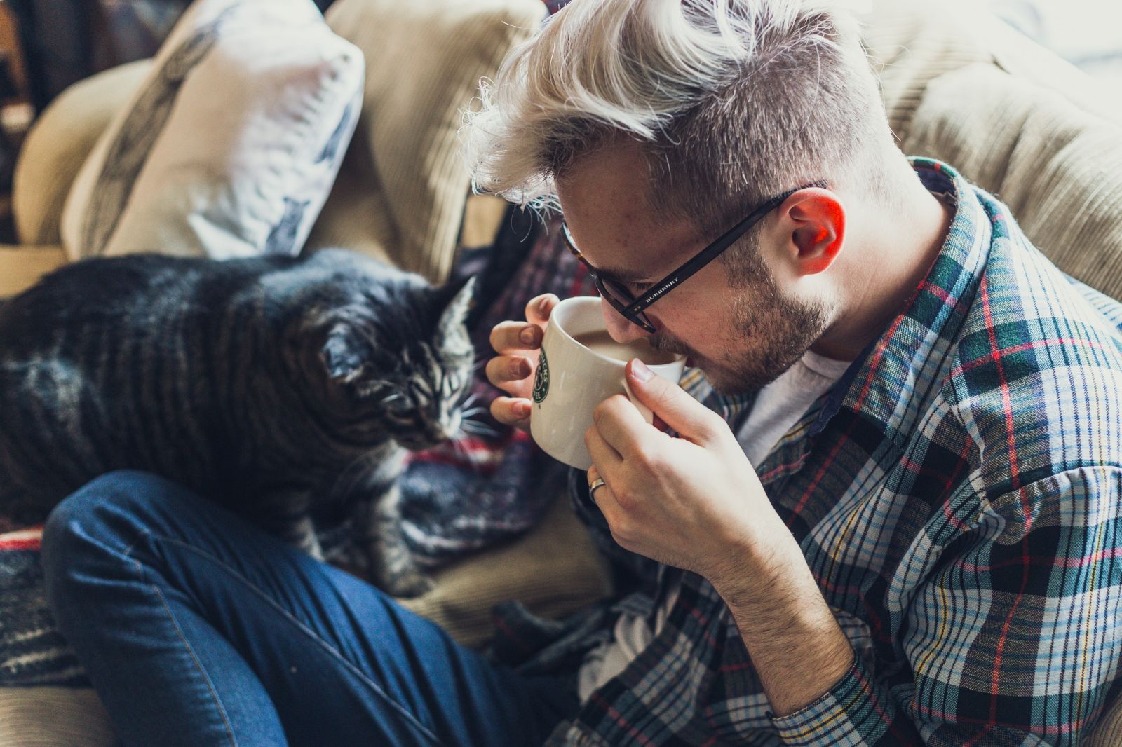 man drinking coffee on couch with cat